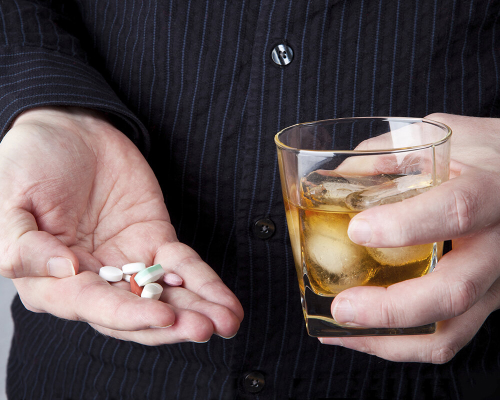 Таблетки и алкоголь в руке